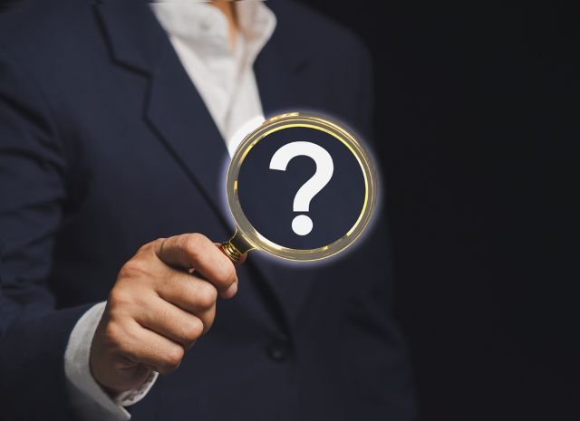 ハテナマークが書かれた虫眼鏡を持つ男性