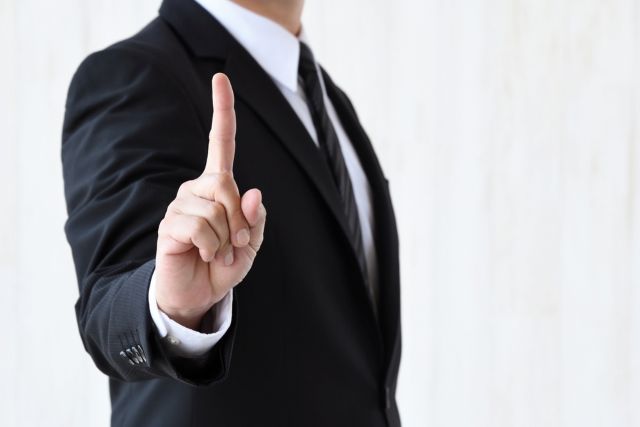 人差し指を上に向けるスーツの男性